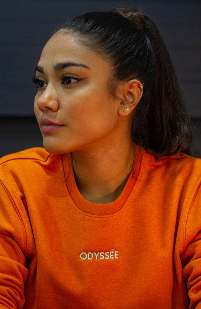 Sweat Shirt Odyssée Orangé, le logo odyssée brodé sur la poitrine, porté par une fille au cheveux noir